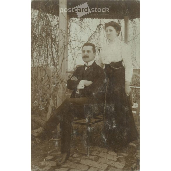 1910 – Full-length photo of husband and wife in the garden. The setting is a bit stiff, revealing a lot about the couple’s relationship. Original paper image. Postcard, photo sheet. (2791994