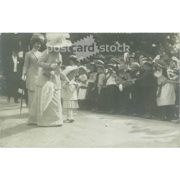 1912 – A distinguished lady with her granddaughter at an event among children. The people in the picture and the creator of the picture are unknown. Postcard, photo sheet. (2792332)